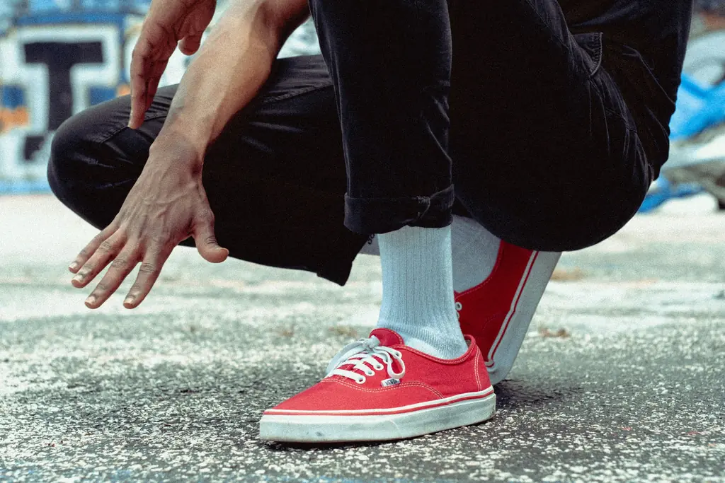 A person crouching on a footpath, holding their ankle