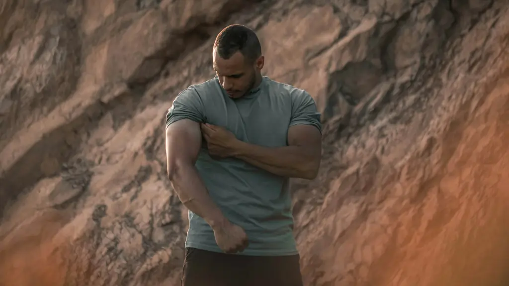A man outdoors holding his upper arm and shoulder