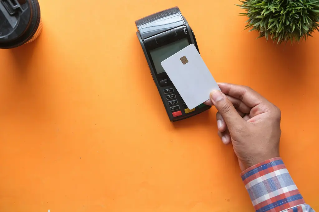 A hand holding a card next to a payment terminal