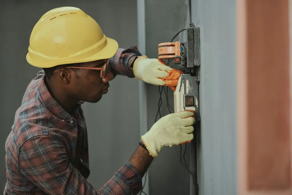 An electrician in a hard hat and gloves working on a switchboard
