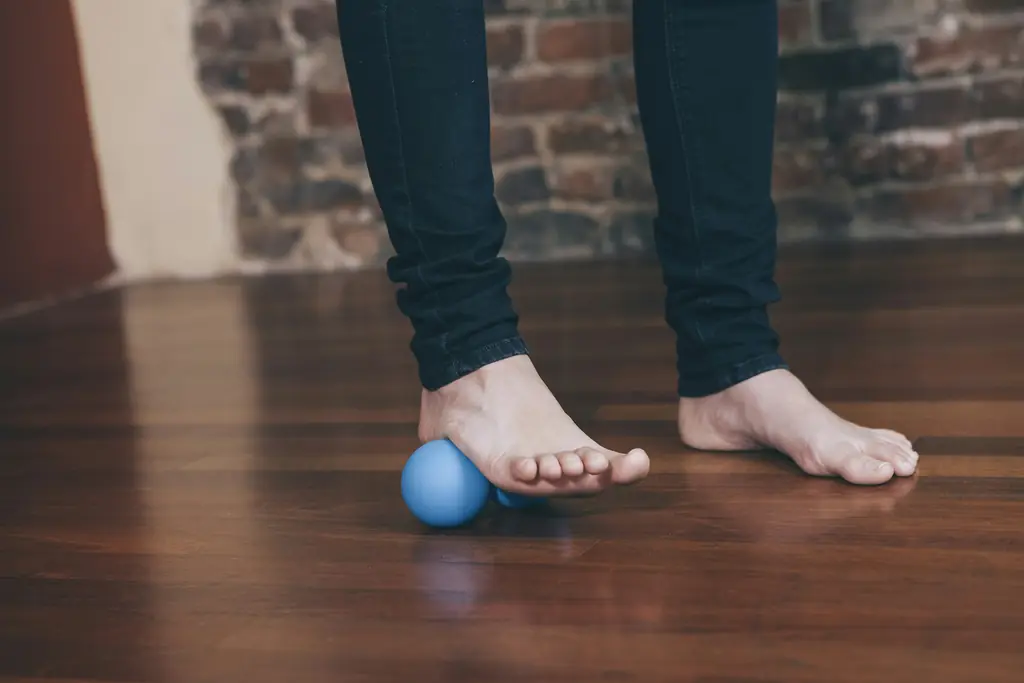 A bare foot rolling a small massage ball on a timber floor