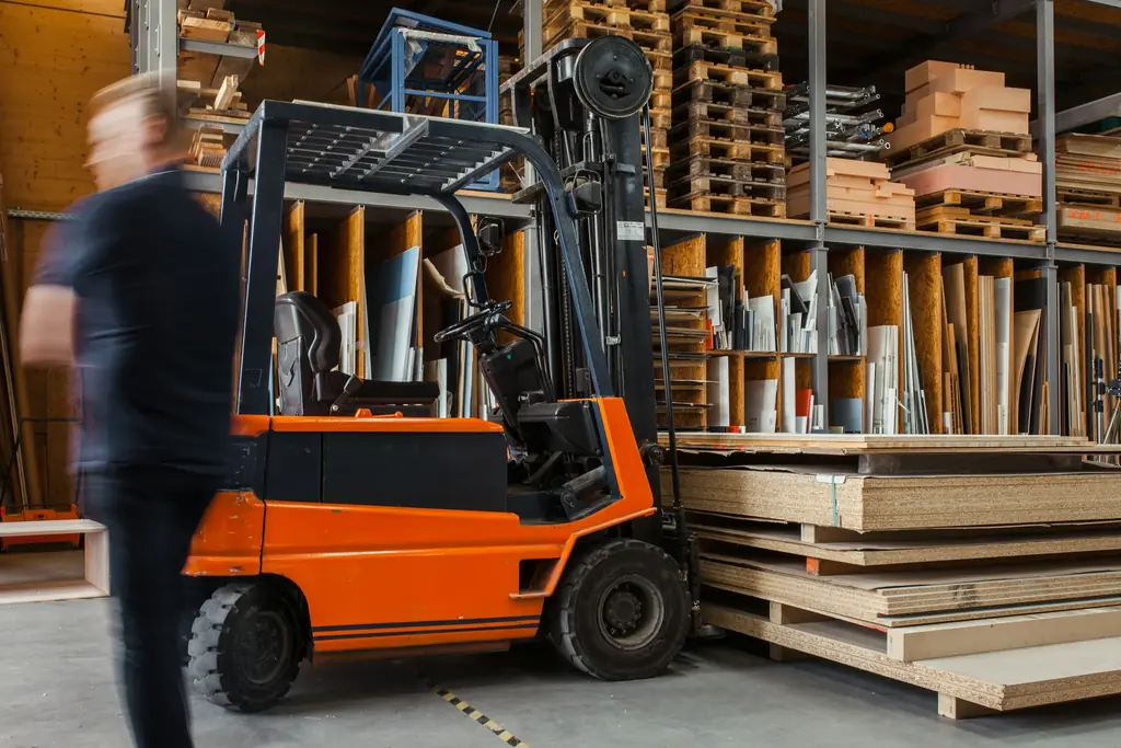 A forklift in a timber yard with a worker walking past