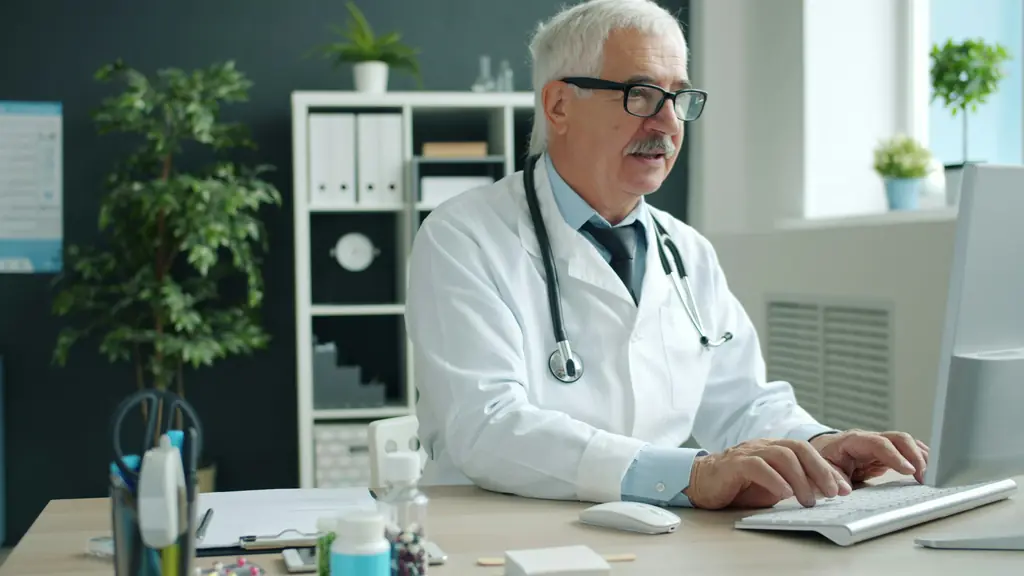 A doctor with a stethoscope typing at a desk computer