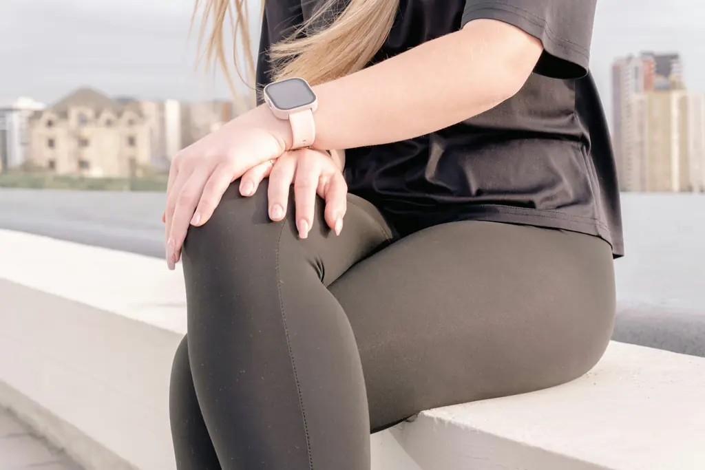 A person in leggings sitting outdoors, holding their knee