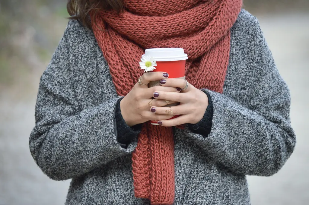 A person in a scarf and coat holding a hot drink