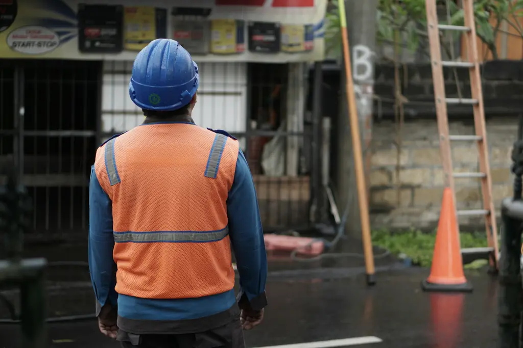 A worker in a hard hat and high visibility vest, seen from behind