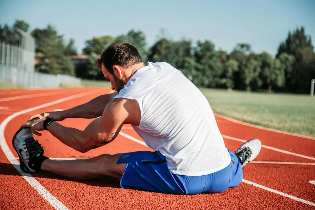 A man stretching his hamstring on a running track
